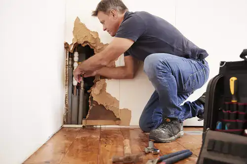 Middle aged man replacing water pipe inside the broken wall