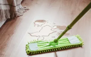 Cleaning up a water leak on the wooden floor with a green mop
